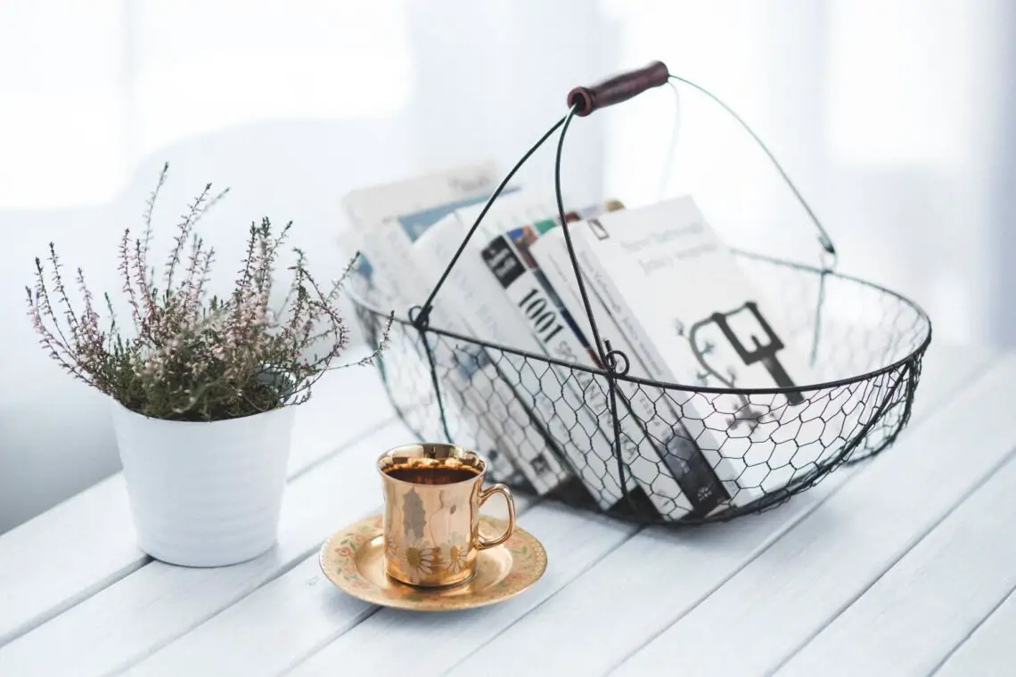 a wire basket filled with best books for migraine with a copper cup and saucer in front and a plant in a white planter on a white slatted table