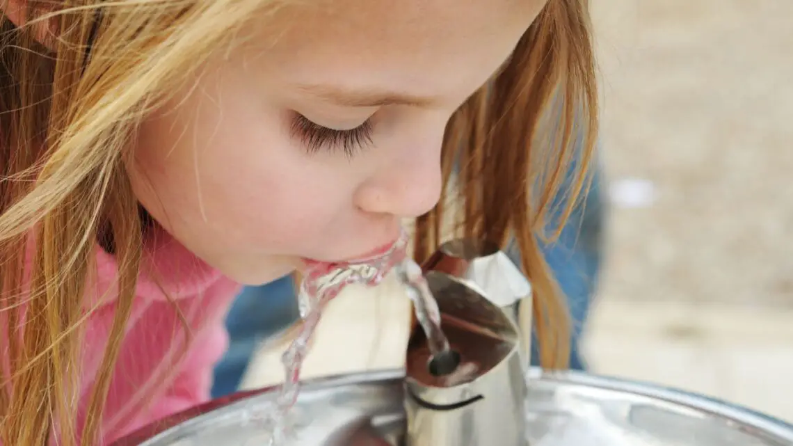 young girl drinking from a water fountain for DoesDrinking Water Help Migraine blog